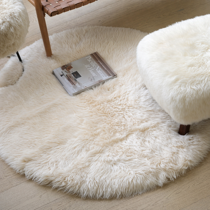Fluffy sheepskin ivory rug on a wooden floor with a book and chair partially visible.